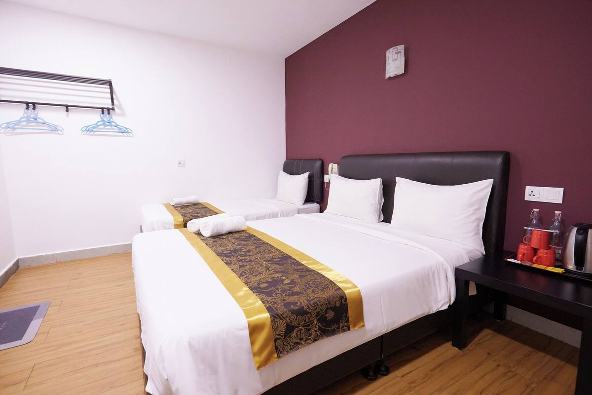 A hotel room with two beds, a wooden floor, a wall-mounted drying rack, and a bedside table with a kettle and cups.
