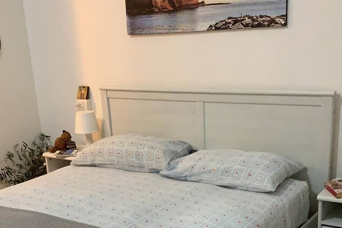 Una cama bien hecha con ropa de cama estampada, una lámpara de noche y un cuadro en la pared.