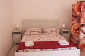Un lit bien fait, avec une literie à motifs floraux, deux oreillers et des serviettes pliées, le tout posé sur une tête de lit blanche.