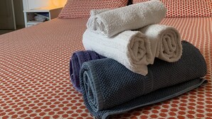 Ein ordentlich bezogenes Bett mit einer gemusterten Tagesdecke, ein aufgerolltes Handtuch und ein gefaltetes Handtuch darauf.