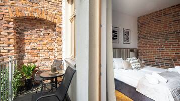 A room with a brick wall, a bed with white bedding, and a small table with chairs.