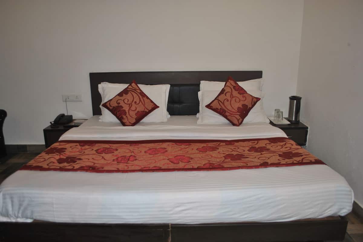 A double bed with a floral bedspread, two decorative pillows, a bedside table with a lamp, and a wall socket.
