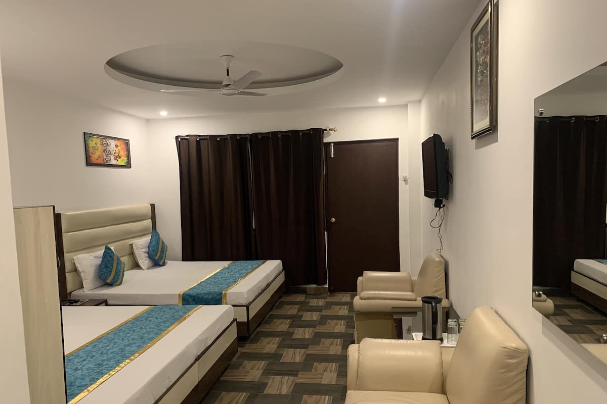 A hotel room with two beds, a sofa, a ceiling fan, a TV, and a door.