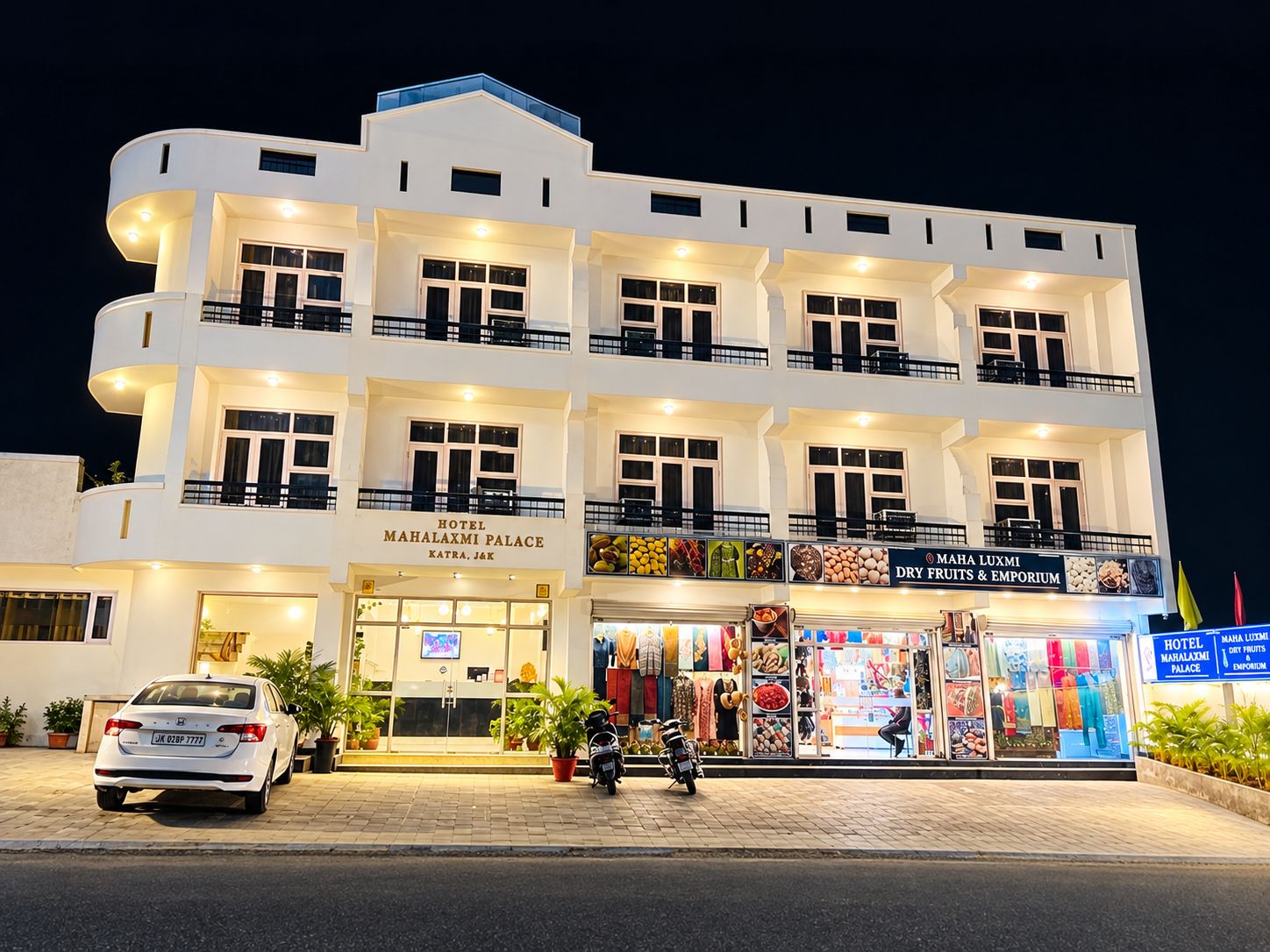 A multi-story hotel with a ground-level dry fruits and emporium, a visible car, and a motorcycle parked in front.