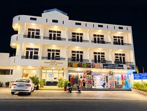 A multi-story hotel with a ground-level dry fruits and emporium, a visible car, and a motorcycle parked in front. - Hotel Maha Luxmi Palace (Reasi)