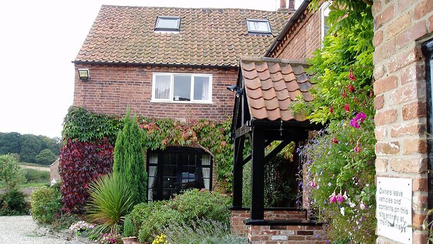 A brick house with a tiled roof, a black door, and a small porch with a sign. - The Barns Country Guesthouse (Retford)