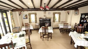 A dining area with wooden chairs and tables, a fireplace, and a clock on the wall. - The Barns Country Guesthouse (Retford)