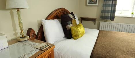 A neatly made bed with a wooden headboard, a bedside table with a lamp, and a window with curtains.