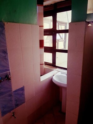Un baño pequeño con ventana, lavamanos y paredes con azulejos.