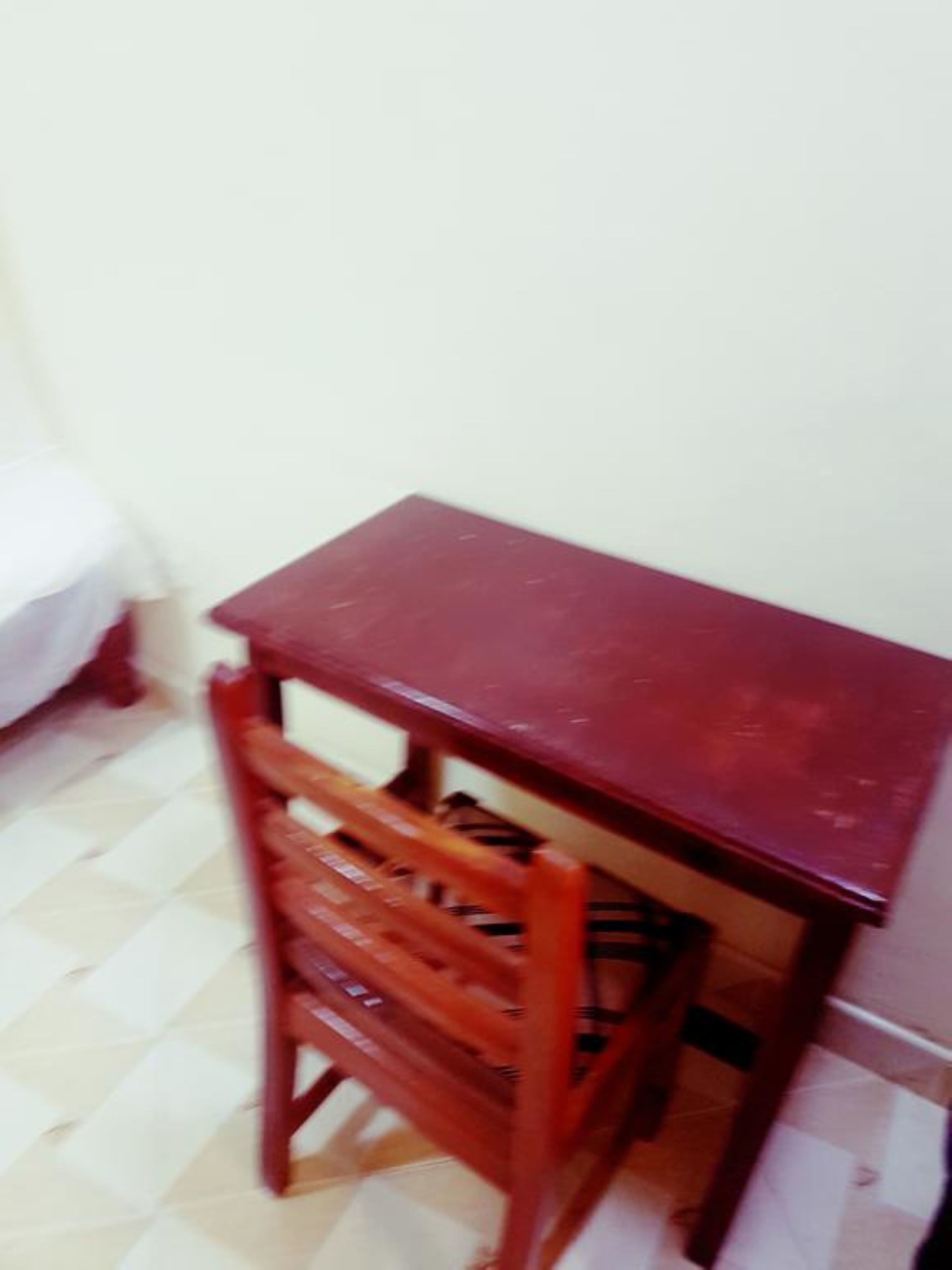 A small wooden desk with a chair in a room with a tiled floor.