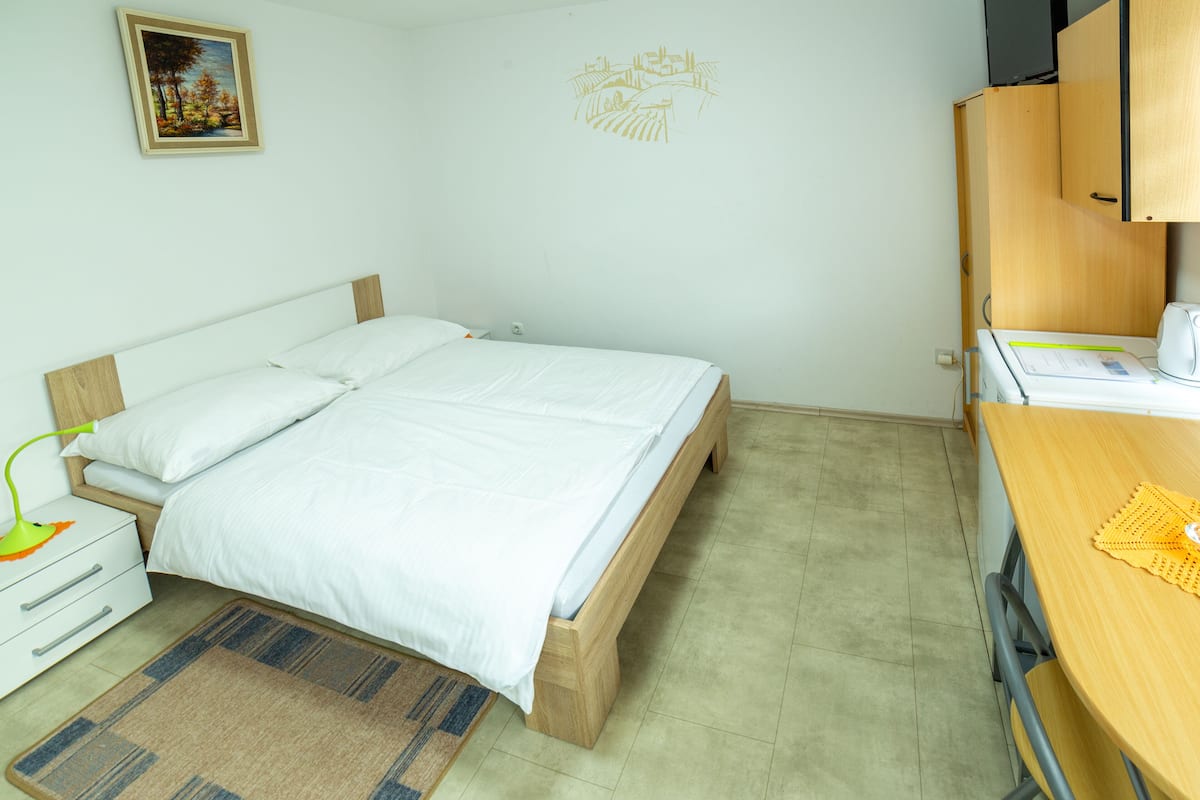 A bedroom with a bed, bedside table, lamp, and a desk with a chair.
