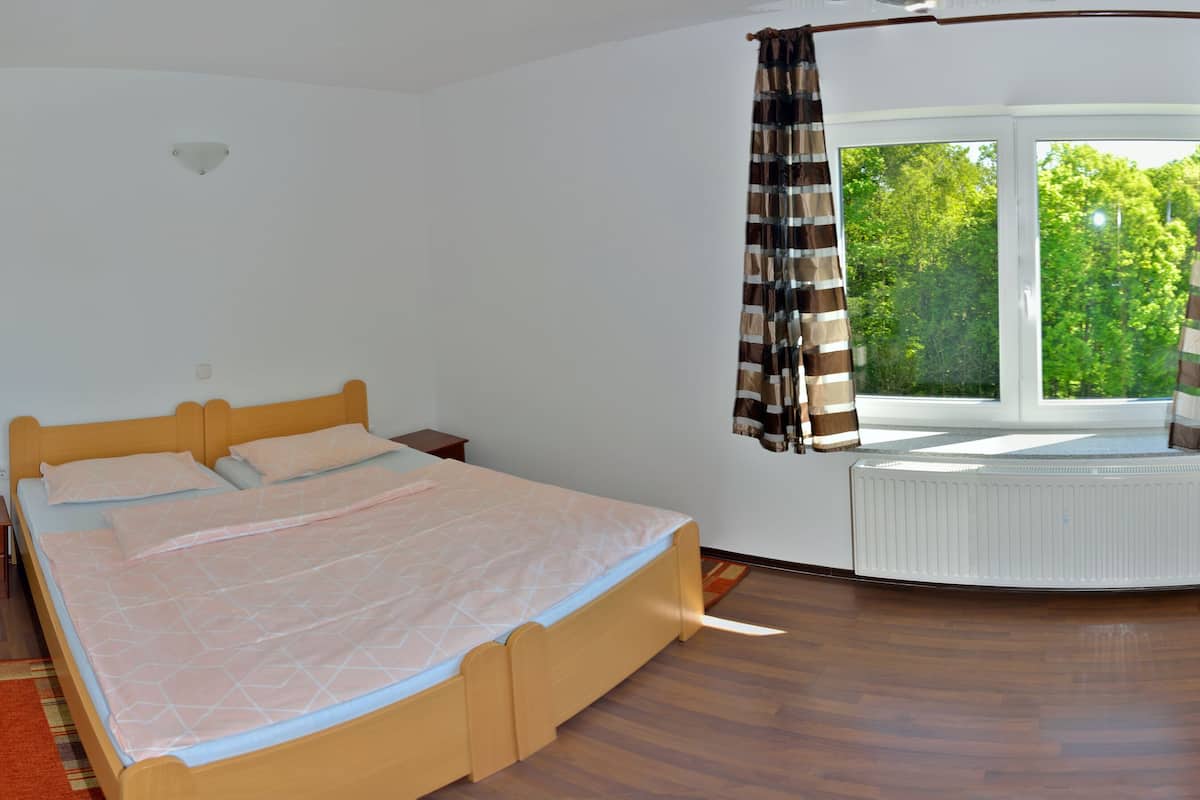 A bedroom with a bed, a window with curtains, a radiator, and a wooden floor.