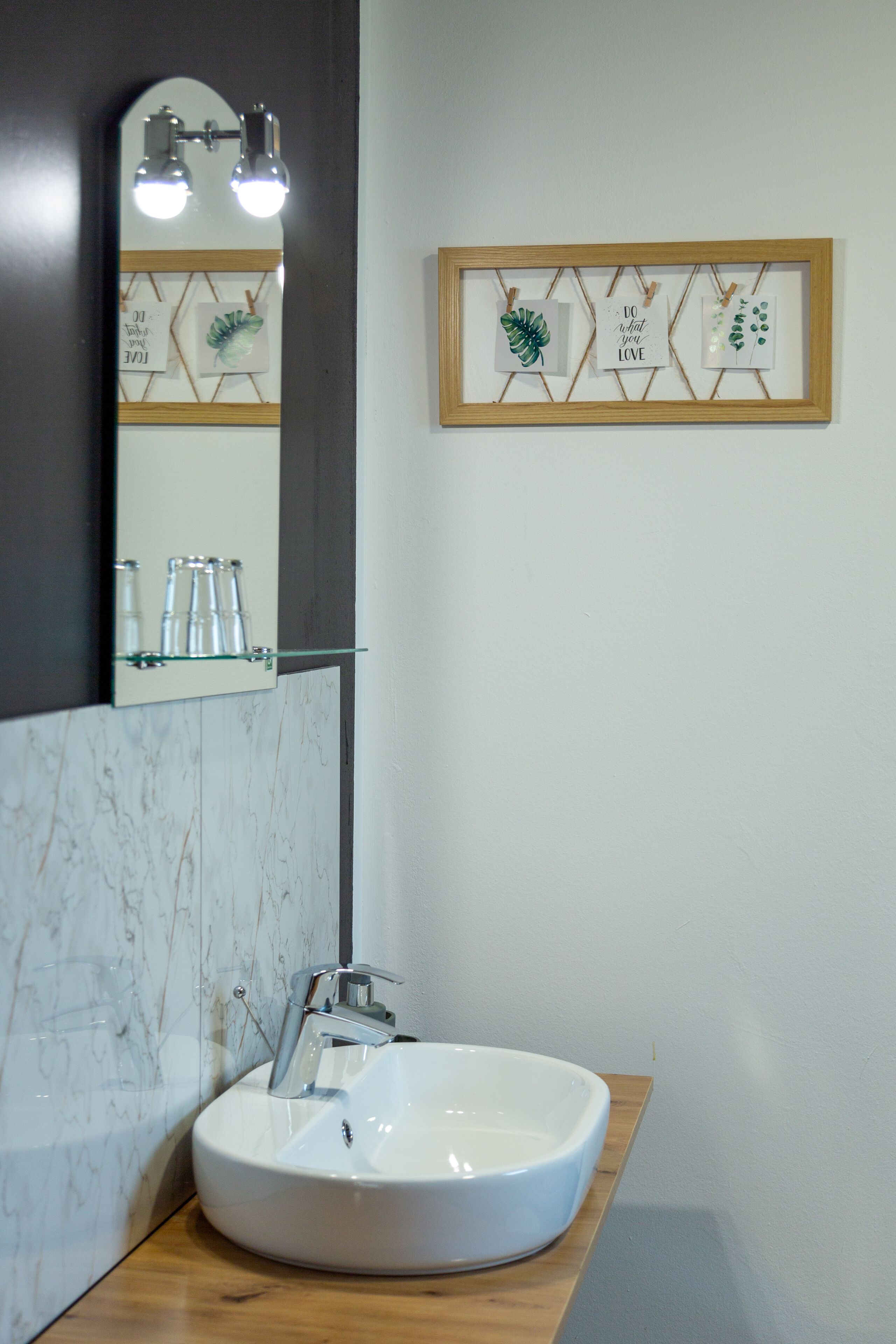 A bathroom with a white sink, a mirror with lights, and framed botanical art on the wall.