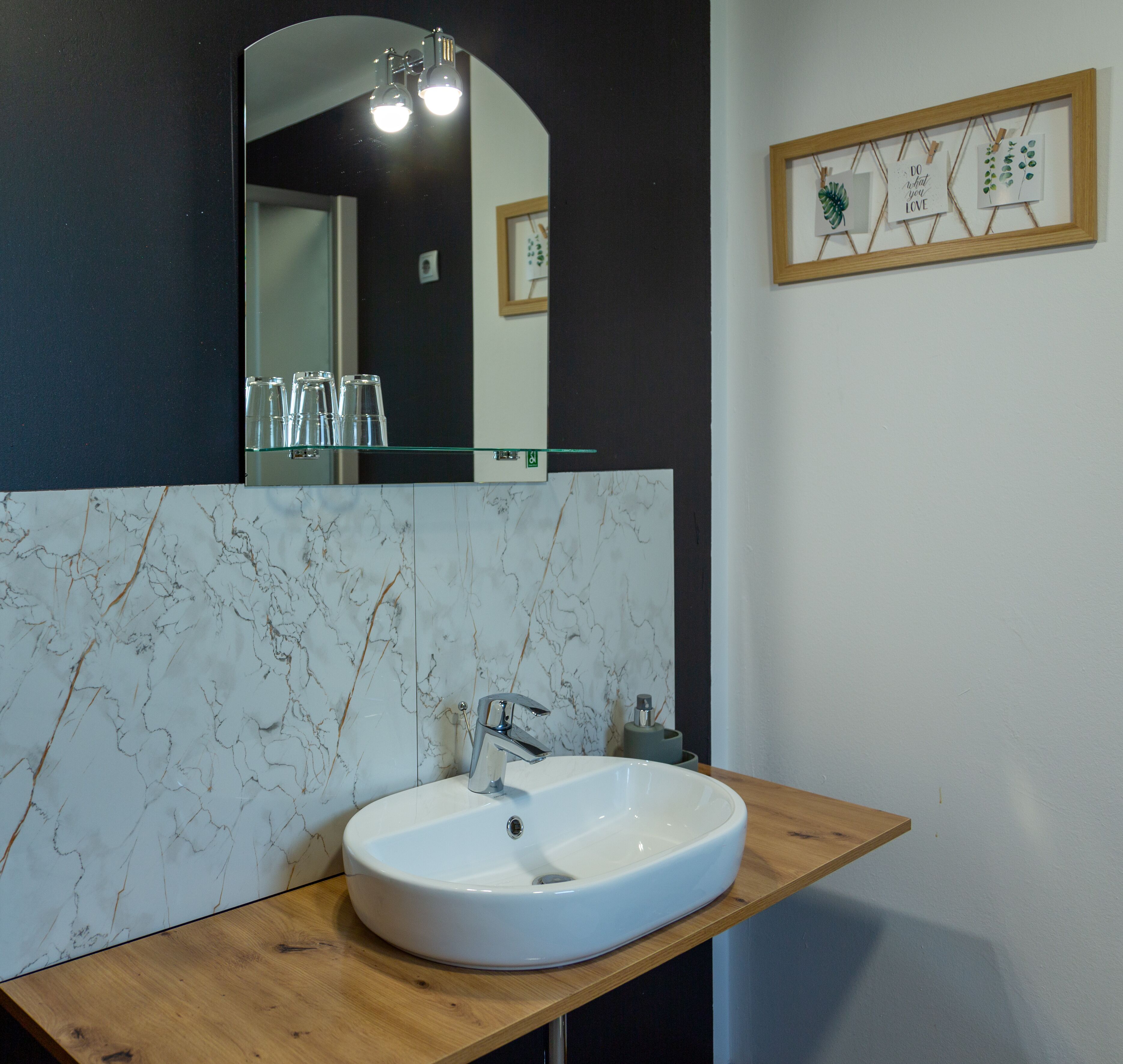 Un bagno con rivestimento in marmo, piano di lavoro in legno, lavandino bianco e specchio soprastante.