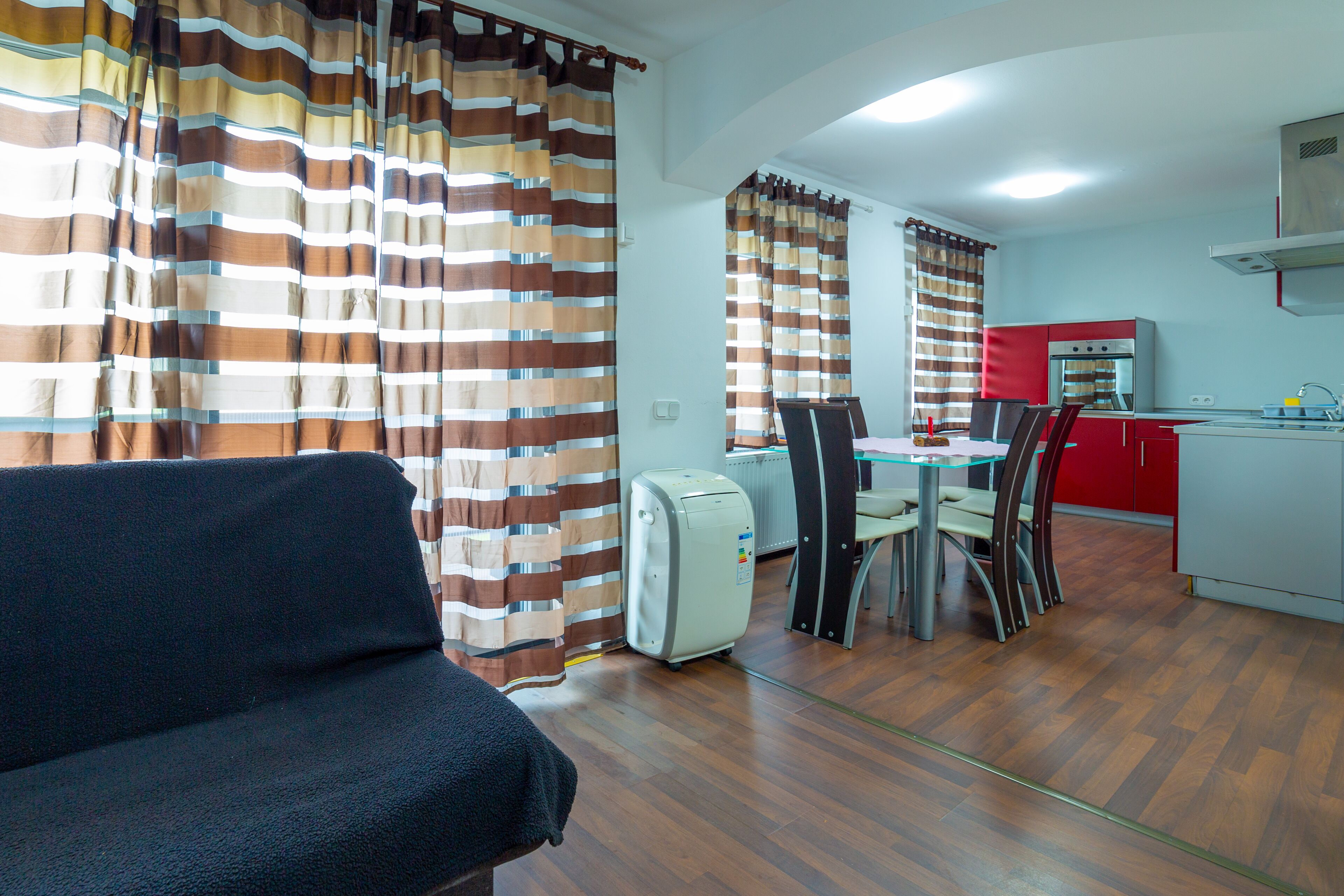 A compact living space with a sofa, a dining table with chairs, a kitchenette, and striped curtains.