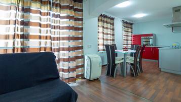 A compact living space with a sofa, a dining table with chairs, a kitchenette, and striped curtains.