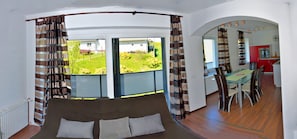 Una habitación con un ventanal grande, un sofá, un comedor y una cocina visible a través de un arco.