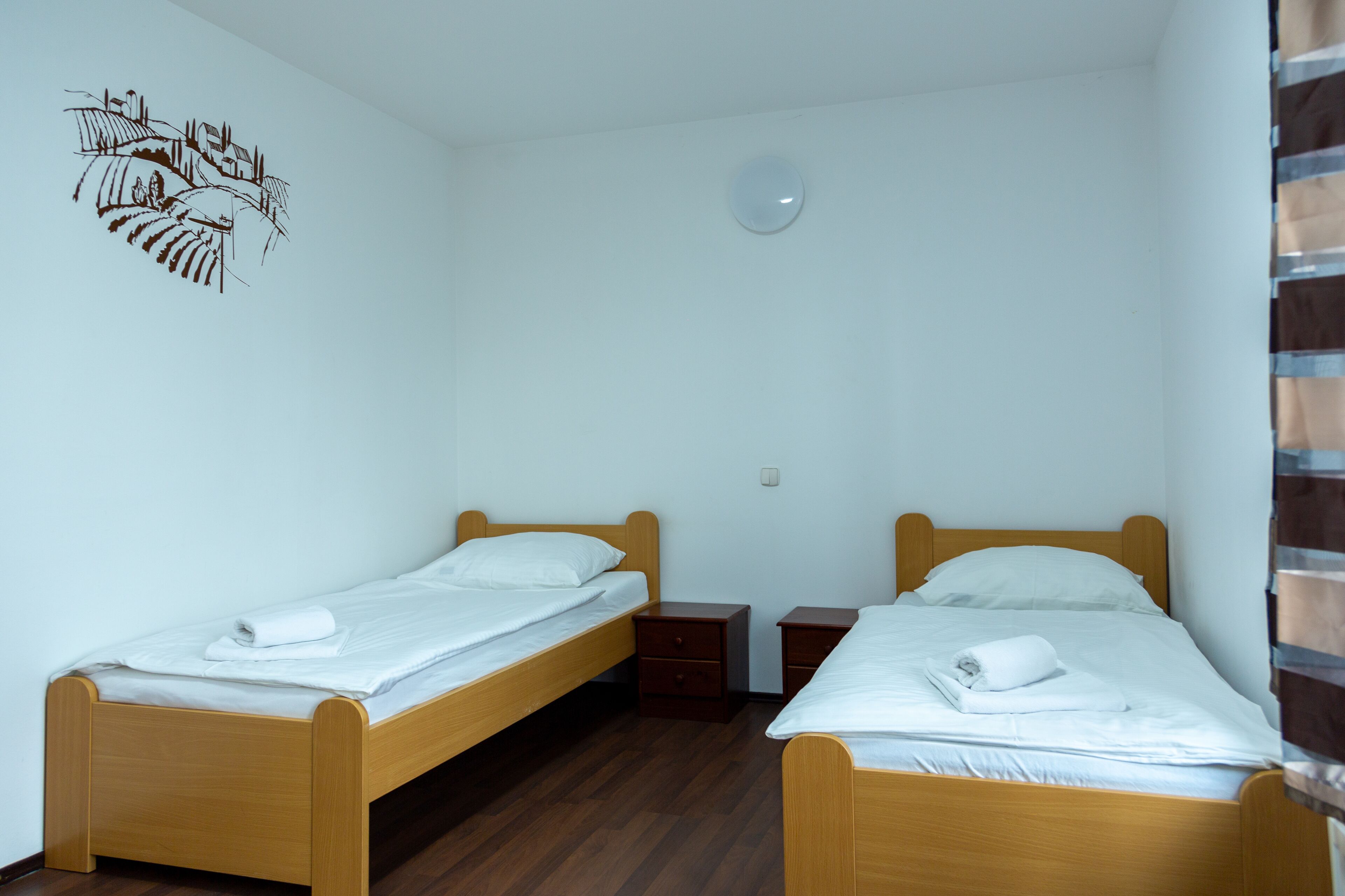A small, clean room with two wooden beds, each with a white mattress and pillows, and a small bedside table.