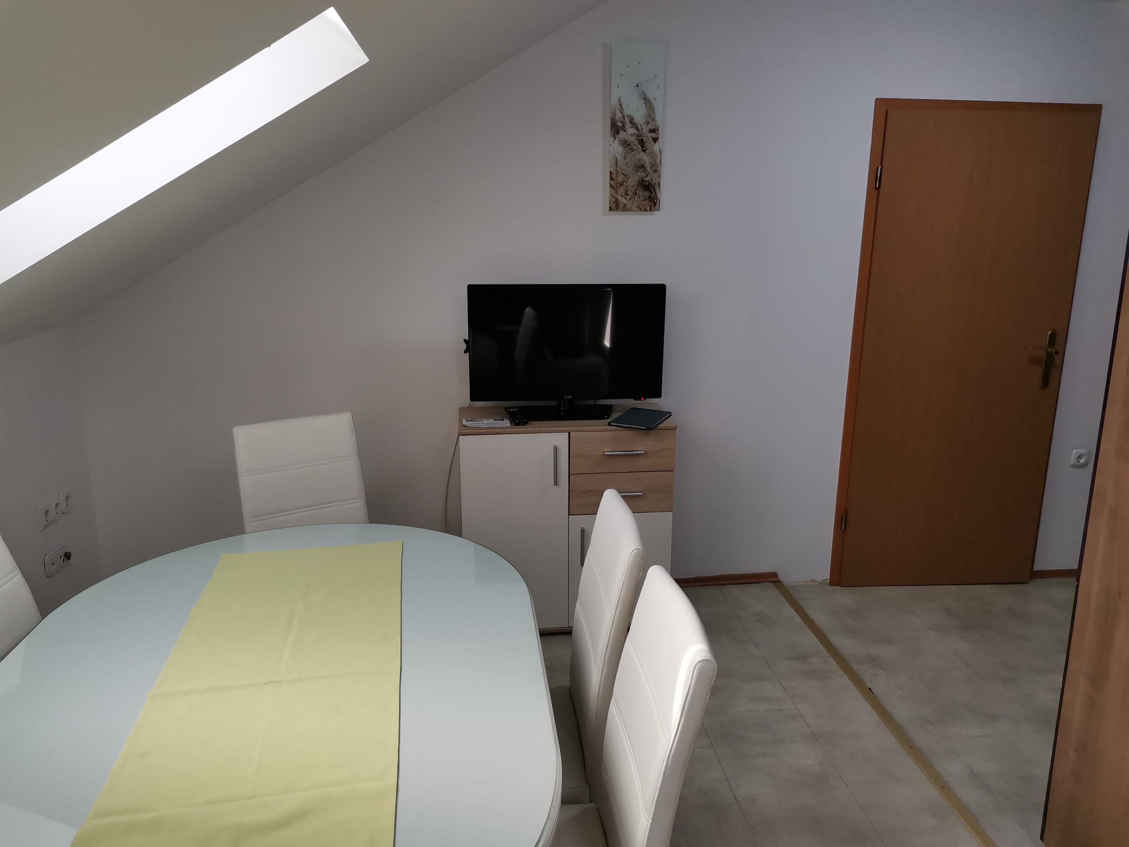 A small, modern room with a bed, a desk, a television, and a door.