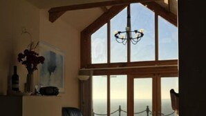 A spacious living room with a large window, a leather sofa, and a chandelier. - Beautiful Wales (Barmouth)