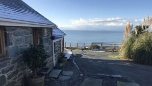 A stone house with a view of the sea, a gravel driveway, and a wooden fence. - Beautiful Wales (Barmouth)