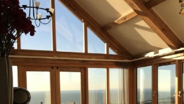 A sunlit room with a view of the sea, featuring a wooden table and chairs, and large glass doors. - Beautiful Wales (Barmouth)