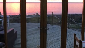 A view through a glass door of a wooden deck overlooking a beach at sunset. - Beautiful Wales (Barmouth)