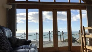 A room with a large sliding glass door leading to a balcony with a view of the sea and a wooden deck. - Beautiful Wales (Barmouth)
