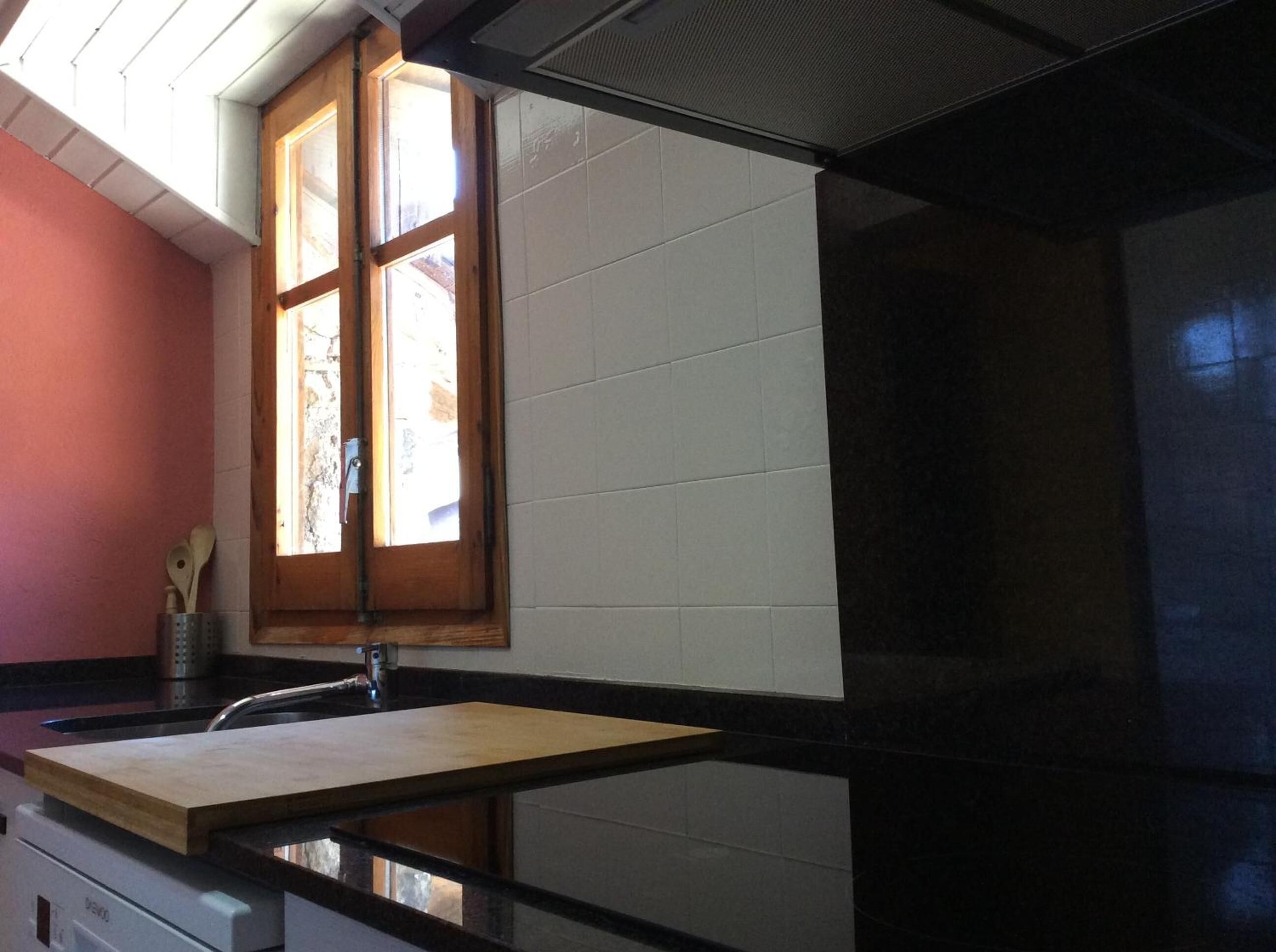 A kitchen with a wooden window, white tiles, and a black countertop.