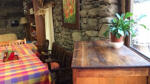 A cozy room with a wooden table and chairs, a bookshelf, a potted plant, and a stone wall. - Casa Rural l'Era de Ferro (La Vall de Boi)