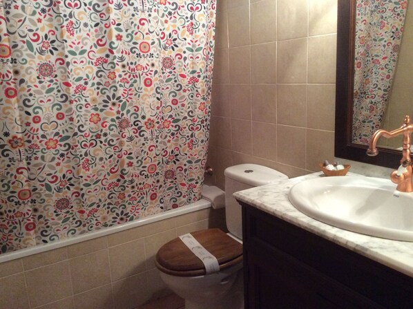 A bathroom with a toilet, a sink, and a shower curtain with a floral pattern. - Casa Rural l'Era de Ferro (La Vall de Boi)
