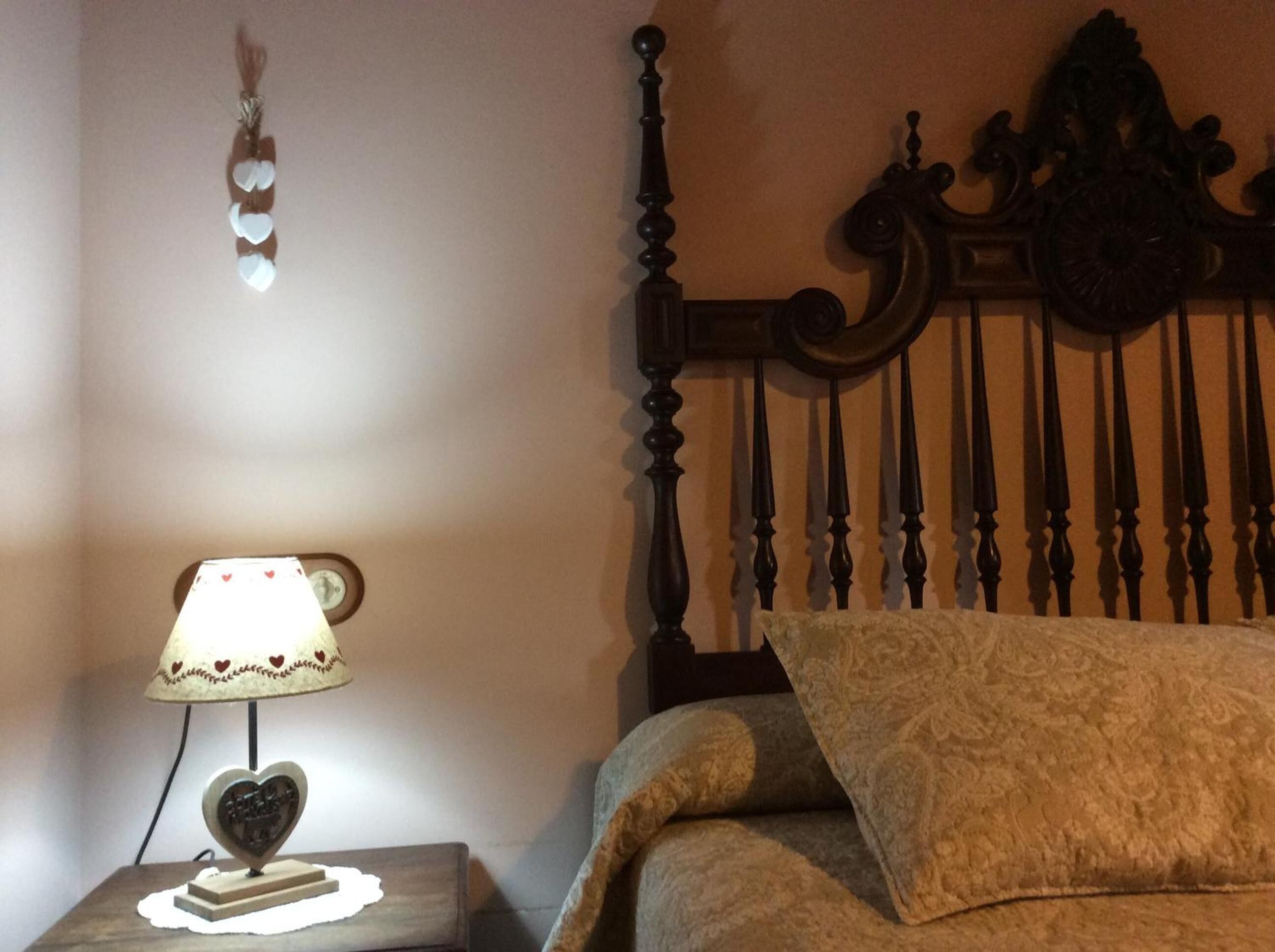 Quarto com cabeceira de madeira, abajur com base em formato de coração e almofada decorativa estampada na cama.
