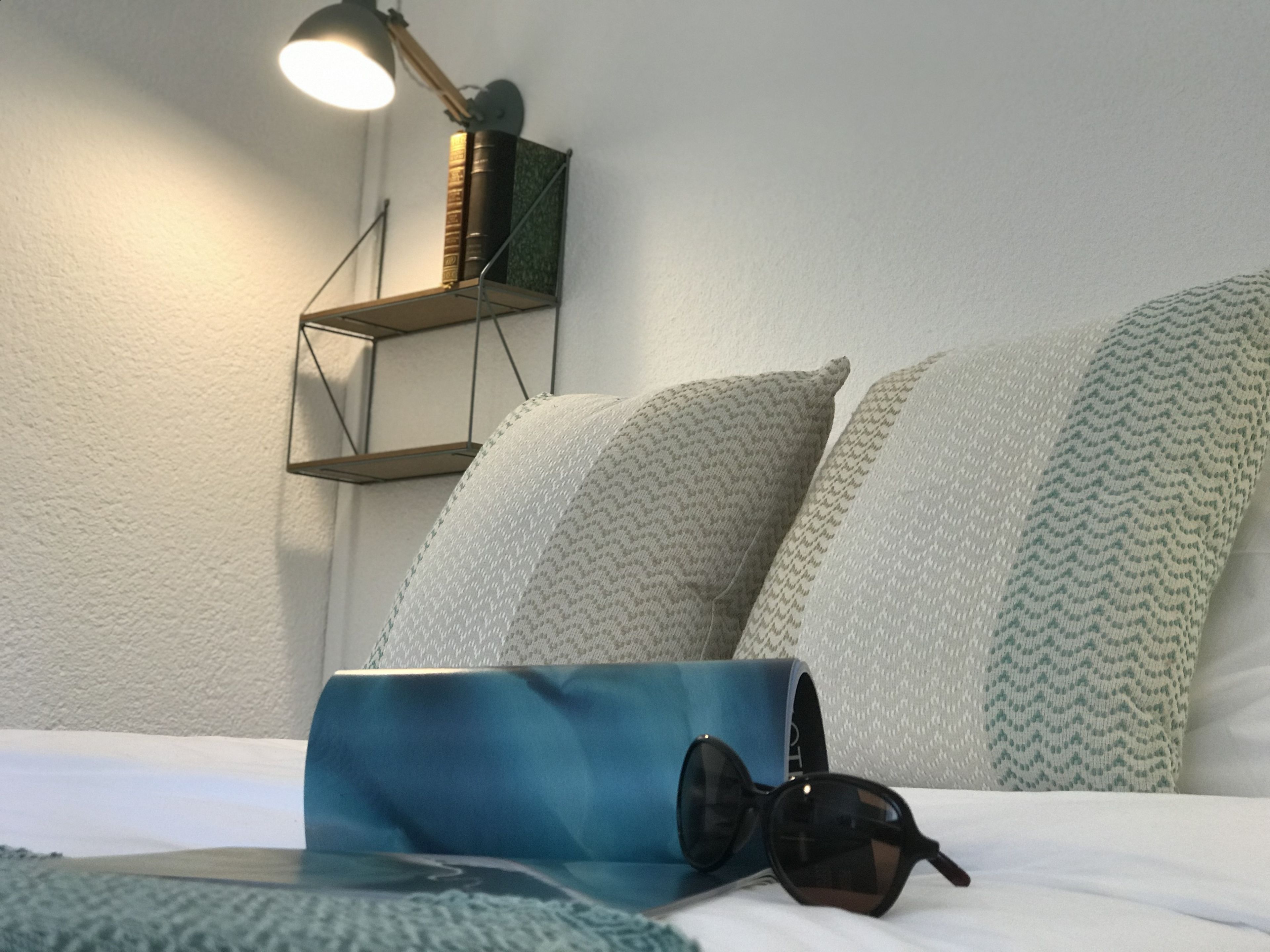 Cama bem arrumada com almofadas, abajur e um par de óculos de sol sobre a cama.
