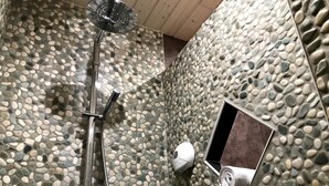 Una ducha con cabezal de ducha de mano y grifo empotrado en una pared con textura de guijarros.