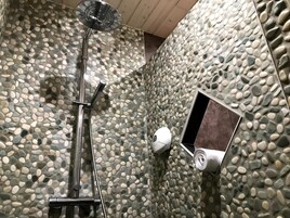 Una ducha con cabezal de ducha de mano y grifo empotrado en una pared con textura de guijarros.
