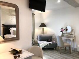 Un dormitorio con cama, escritorio, silla, espejo, lámpara y televisor.