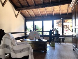 Una habitación acogedora con techo de madera, ventanas amplias, una silla blanca, una mesa de madera y una cesta verde.