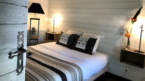 Un dormitorio con cama, mesitas de noche, un espejo, un radiador y una estantería en la pared con una planta.