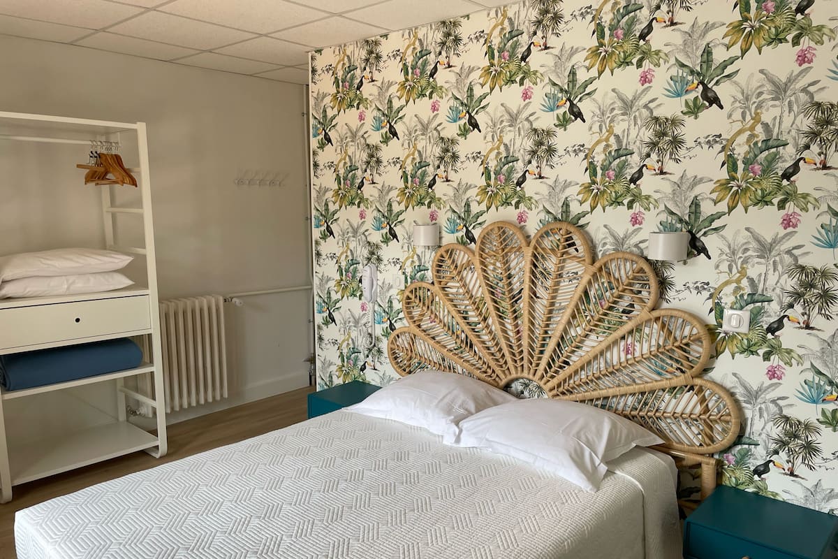 A bedroom with a bed, a wardrobe, a radiator, and a wall with a tropical wallpaper.