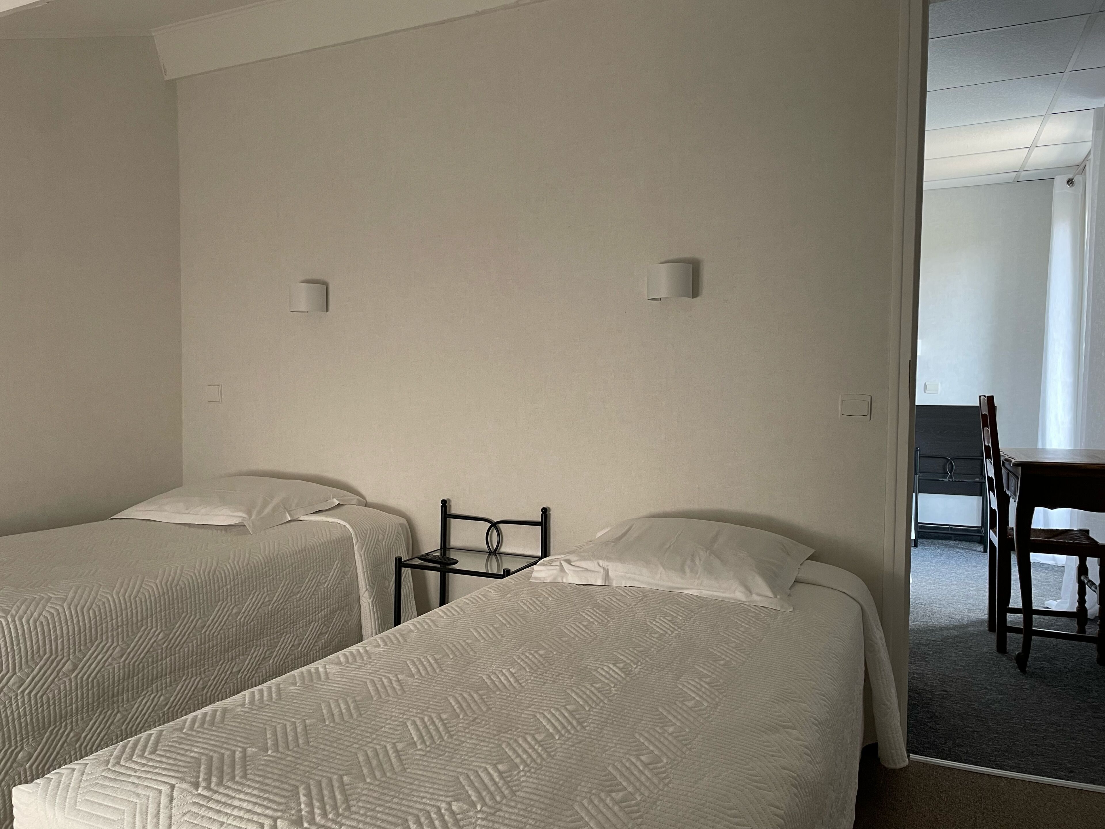 A hotel room with two single beds, a small table, and a chair.