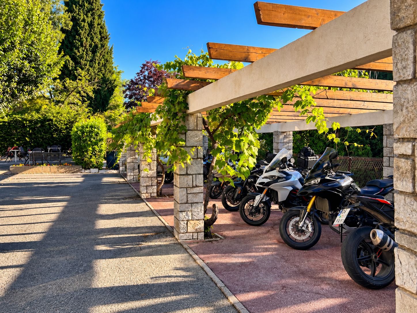 A covered parking area with stone pillars and wooden beams, lined with parked motorcycles.