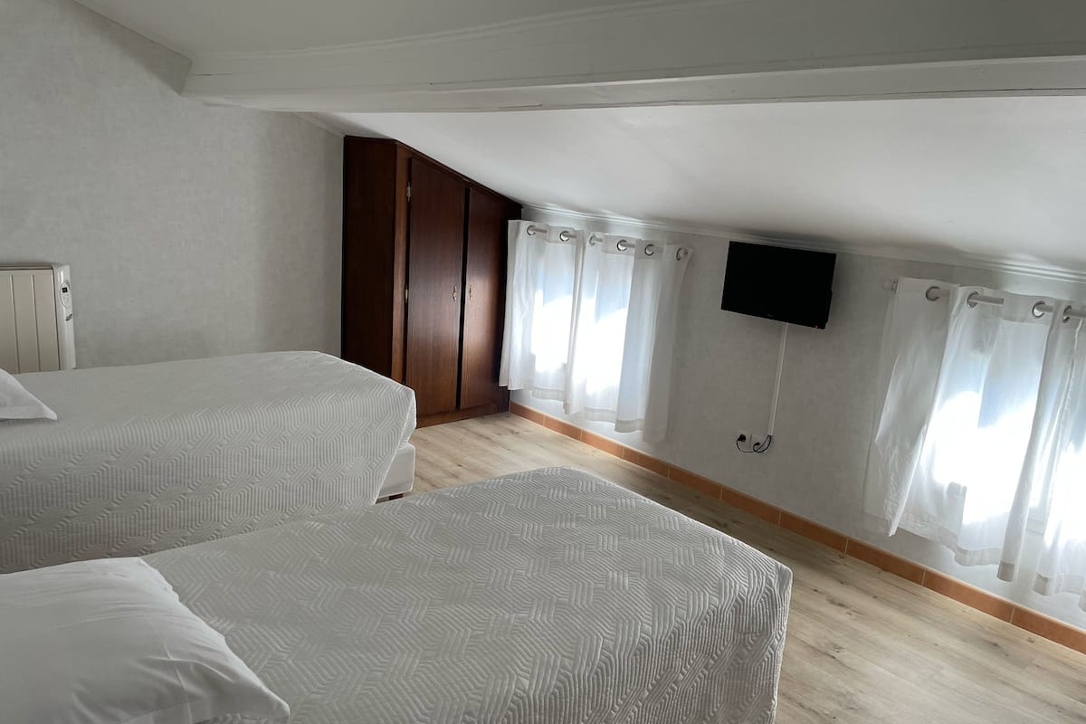 A bedroom with two beds, a wooden wardrobe, a television on the wall, and a window with curtains.
