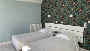 Een slaapkamer met twee bedden, een radiator, een aan de muur bevestigd telefoon en behang met een patroon.