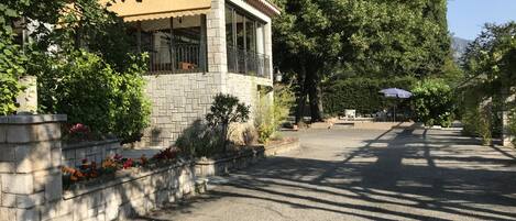 Un edificio de piedra con tejado de baldosas, rodeado de vegetación y un camino de entrada pavimentado.