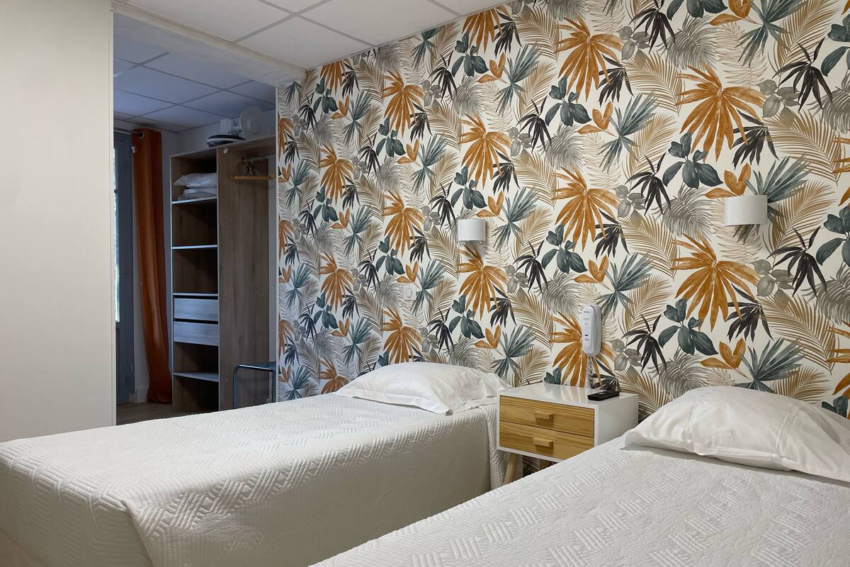 A hotel room with two beds, a wardrobe, and a tropical leaf-patterned wall.