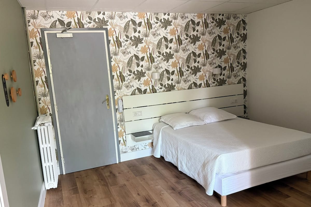 A bedroom with a bed, a radiator, a door, and a wall with a floral pattern.