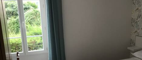 A hotel room with a bed, a window with curtains, and a view of greenery outside.
