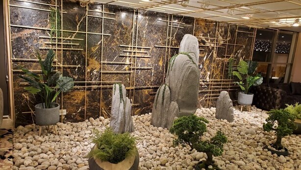 Un jardín interior moderno con formaciones rocosas, plantas en macetas y una pared decorativa.