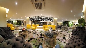 Un amplio vestíbulo con una zona de estar central, sillones tapizados en amarillo y negro, una alfombra estampada y una mesa de vidrio decorativa.