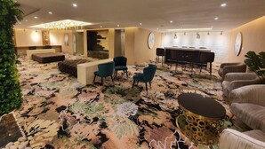 Un moderno vestíbulo de hotel con alfombra estampada, zonas de estar, un mostrador de recepción y un bar.